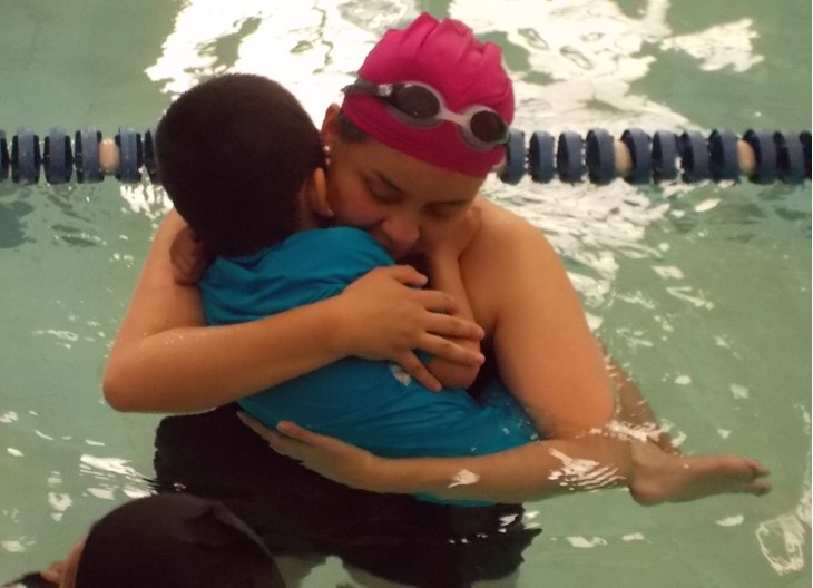 Mujer abraza a niño sobre su pecho estando dentro de la piscina.