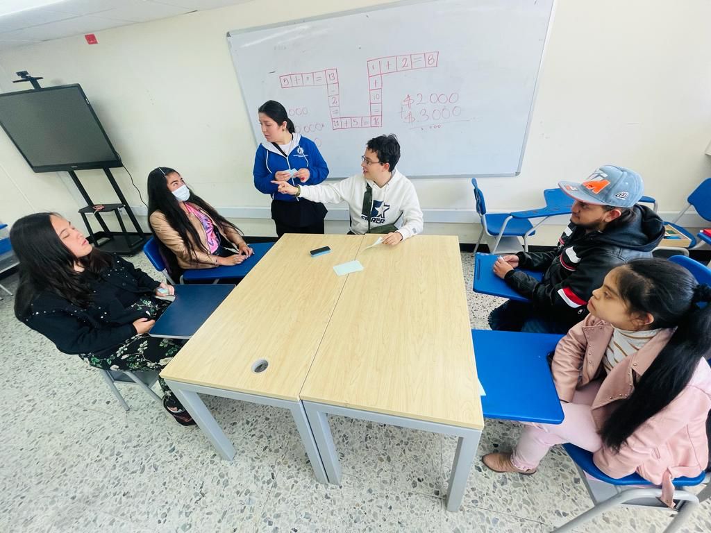 jovenes y niños alrededor de una mesa, interactuan con Licenciada en formación. Escenario en un salón de clase.
